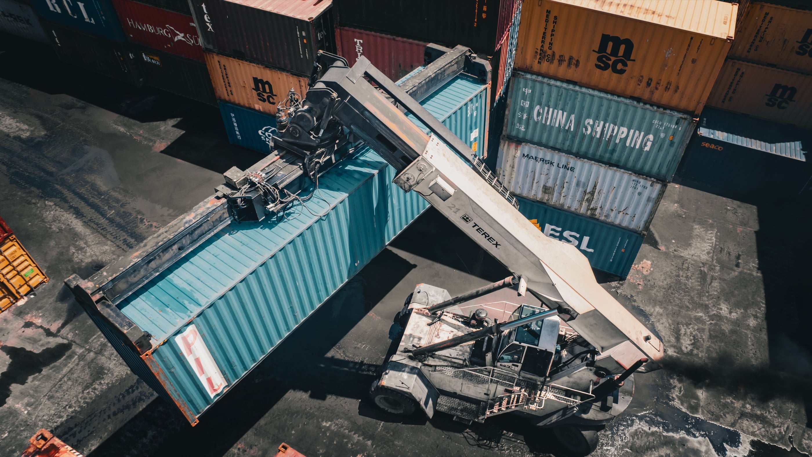 A reach stacker lifting a shipping container among stacked containers at Dar es Salaam port, seen from above.