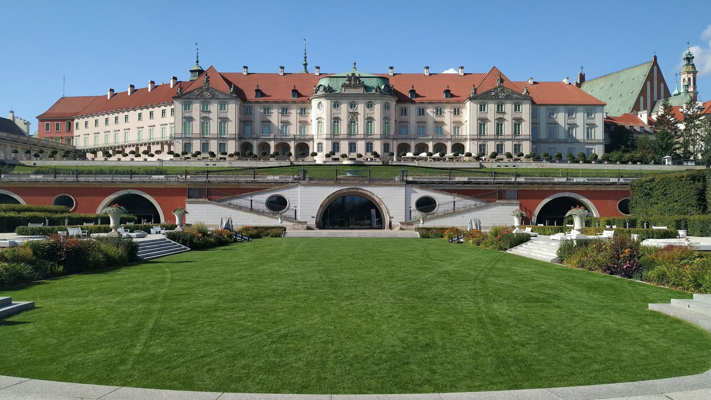 A long pale institutional building across a formal lawn and garden terraces.