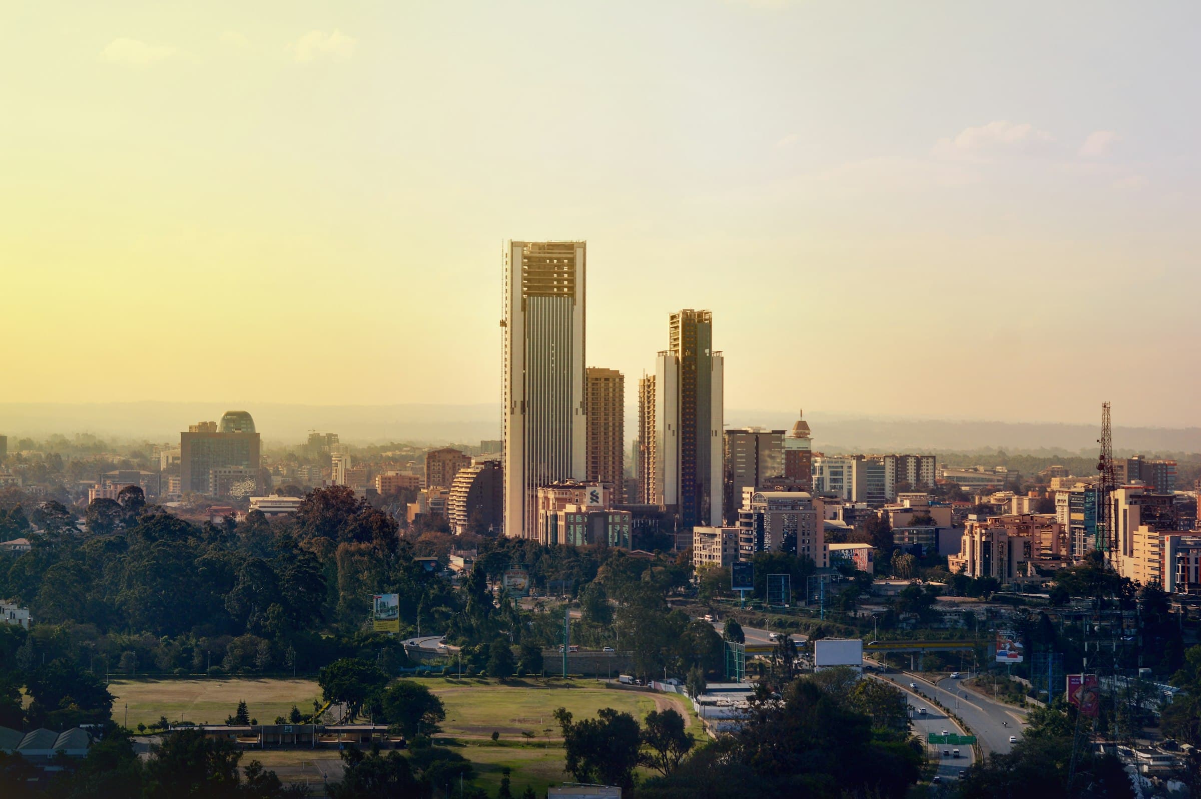 The Nairobi skyline in late light, towers rising above trees and a wide road.